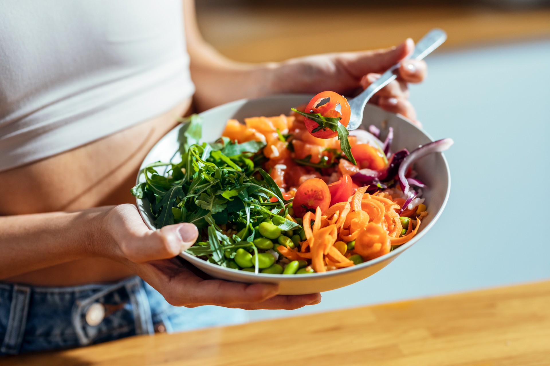 Fitness woman eating a healthy poke bowl in the kitchen at home.